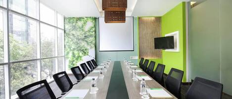 Ein Konferenzraum mit einem langen Tisch, Stühlen, einer Projektionsleinwand und einem Fernseher.
