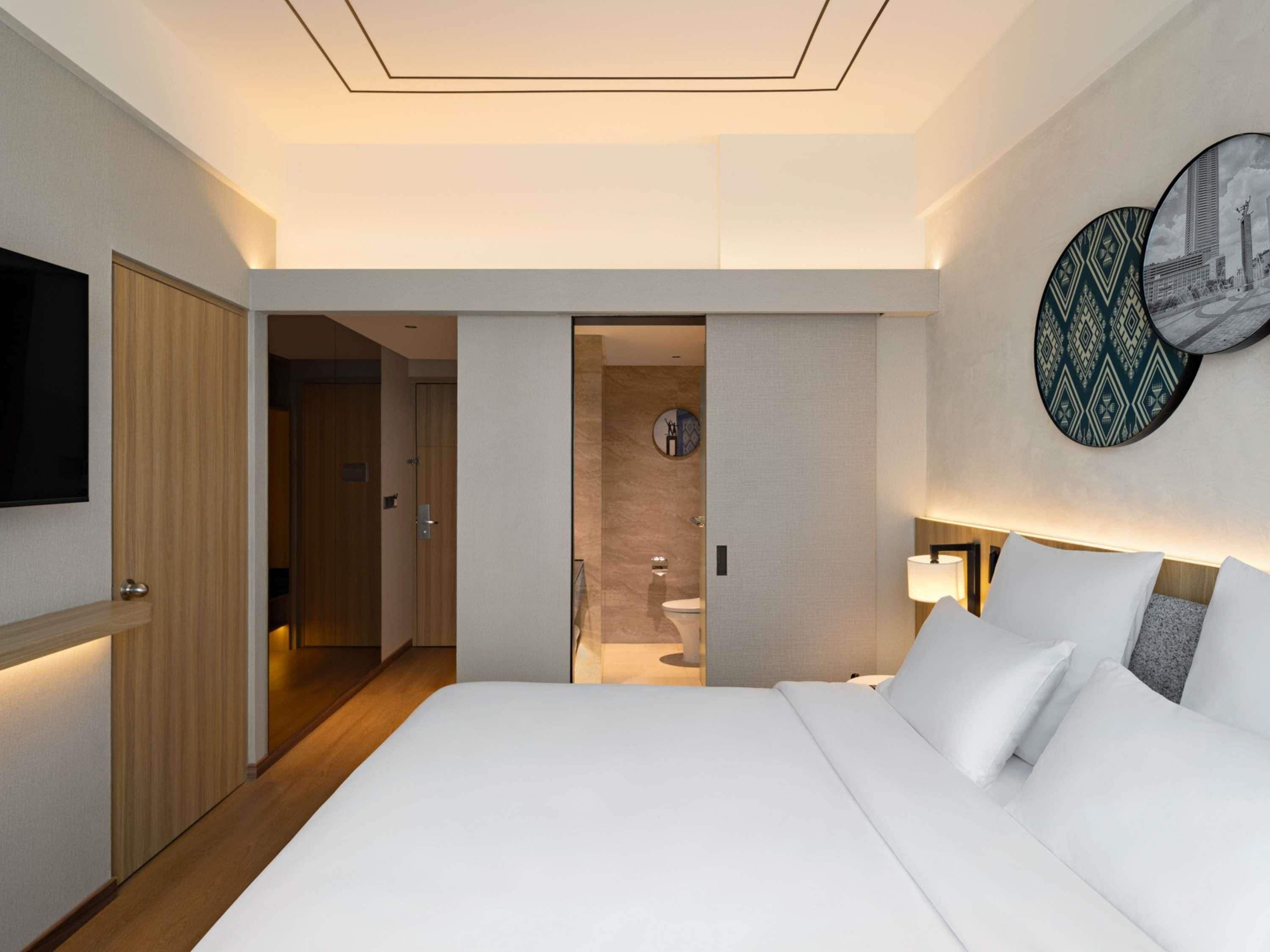 Habitación de hotel con una cama grande, televisión instalada en la pared y baño visible a través de una puerta abierta.