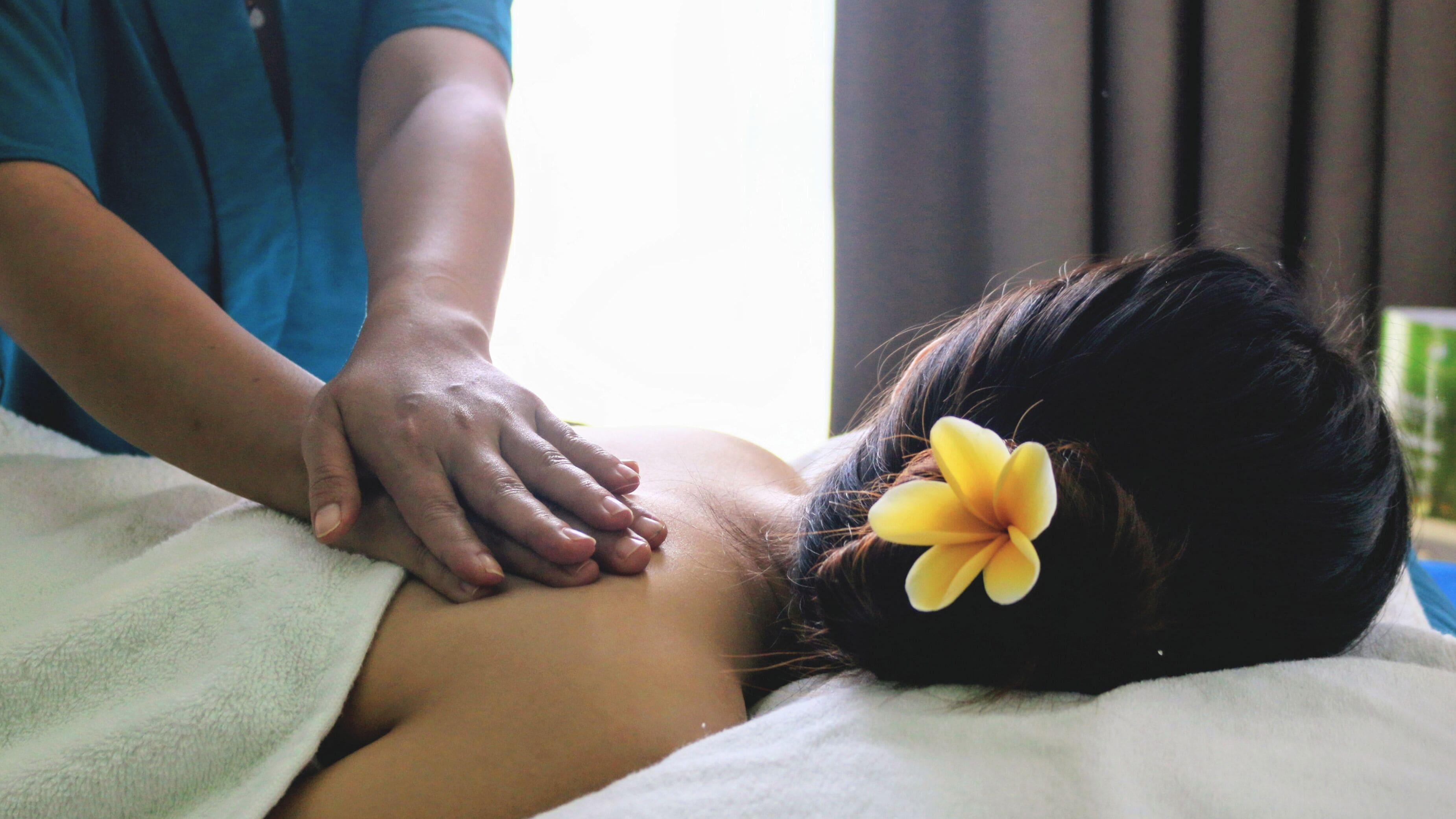 Une personne reçoit un massage, une serviette et un accessoire floral sont visibles.