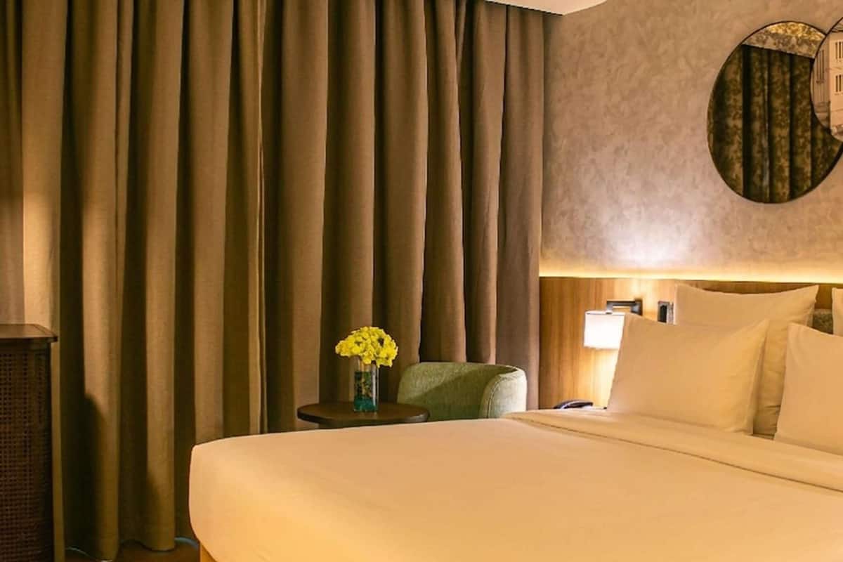 Ein Hotelzimmer mit einem großen Bett, einem Nachttisch mit Blumenvase, einer Lampe und einem grünen Sessel.