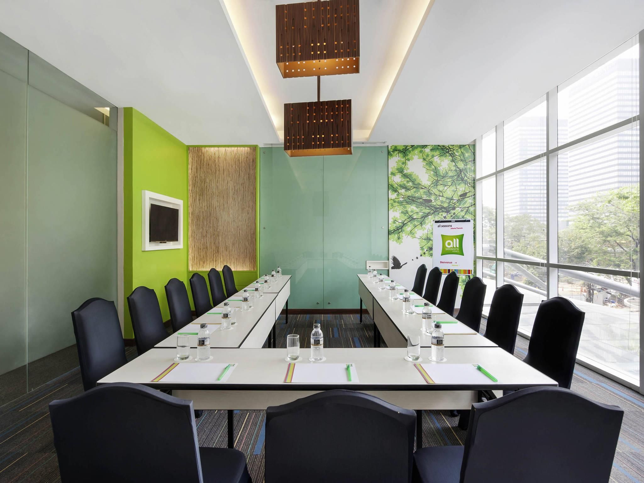 A conference room with a long table, chairs, a projector screen, and a banner.