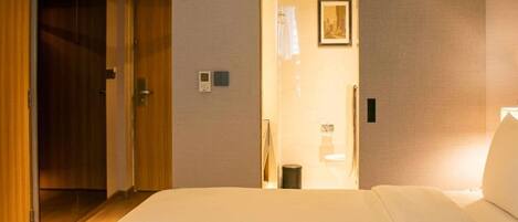 A hotel room with two beds, a wooden door, a bathroom with a shower, and a framed picture on the wall.