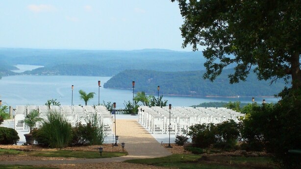 Rows of white chairs arranged for an event, with a pathway leading to a body of water and hills in the background.