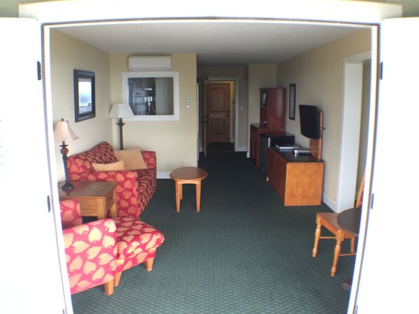 A compact living area with a sofa, a small table, a television, and a kitchenette.