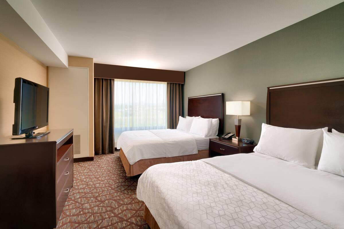A hotel room with two beds, a TV, a desk, and a window with curtains.