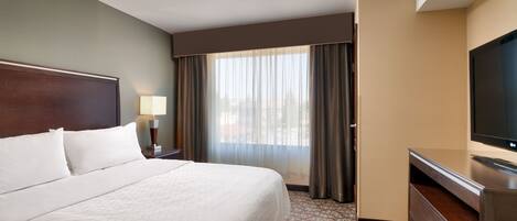 A hotel room with a large bed, a TV on a dresser, a window with curtains, and a lamp on a nightstand.