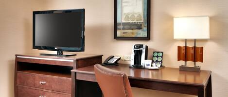 Habitación de hotel con escritorio, televisor, cafetera, teléfono y un cuadro en la pared.