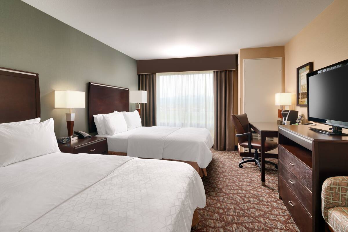 A hotel room with two beds, a desk, a chair, a television, and a window with curtains.