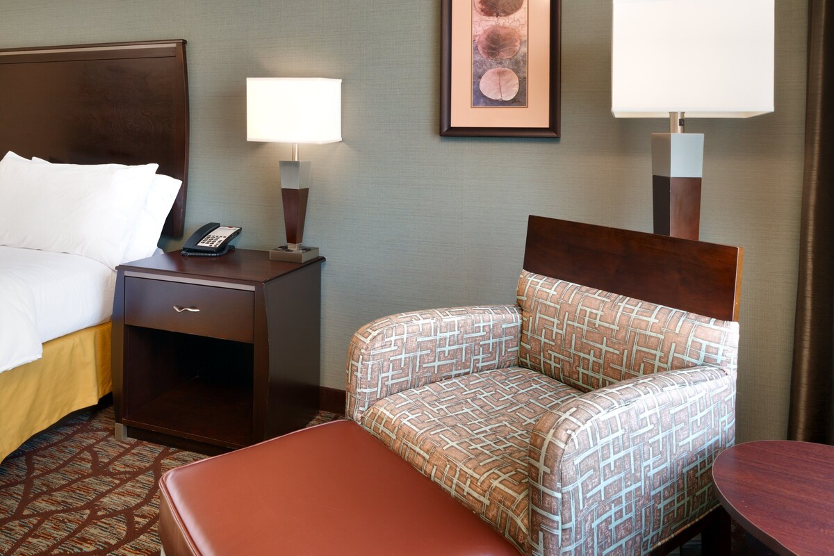 Une chambre d’hôtel avec un lit, une table de chevet avec un téléphone, une lampe, un canapé à motifs et une petite table.