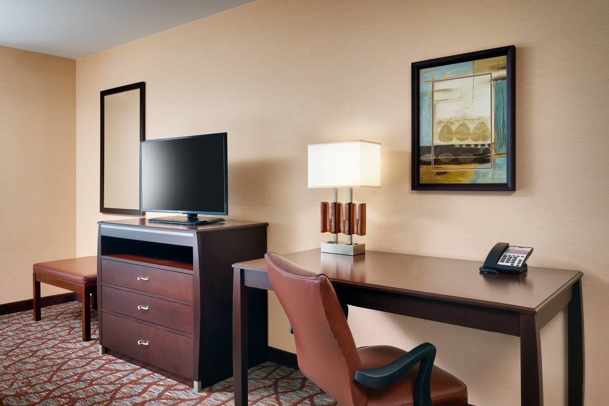 A hotel room with a desk, a television, a lamp, a phone, and a chair.