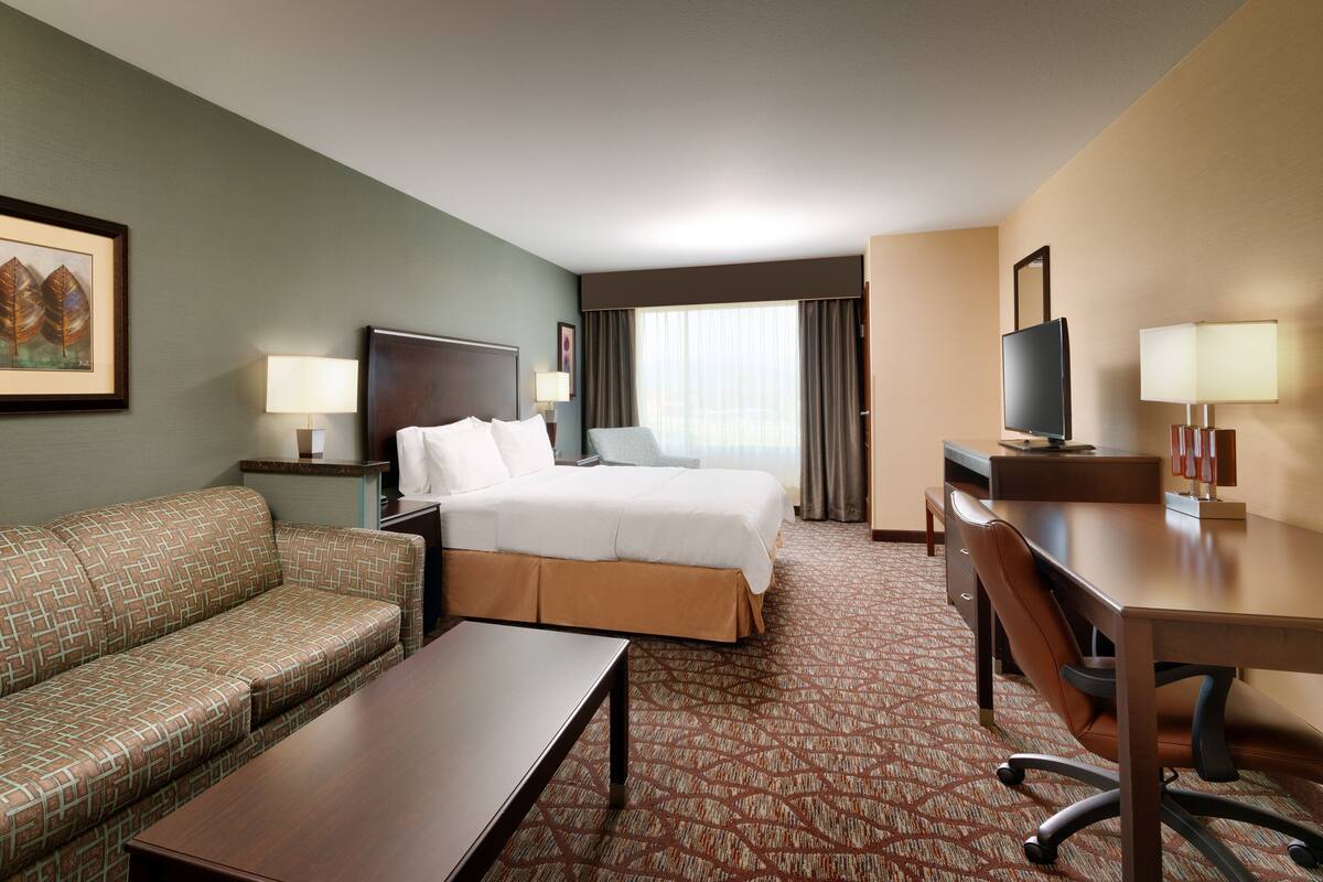 A hotel room with a bed, a sofa, a desk, a TV, and a window with curtains.