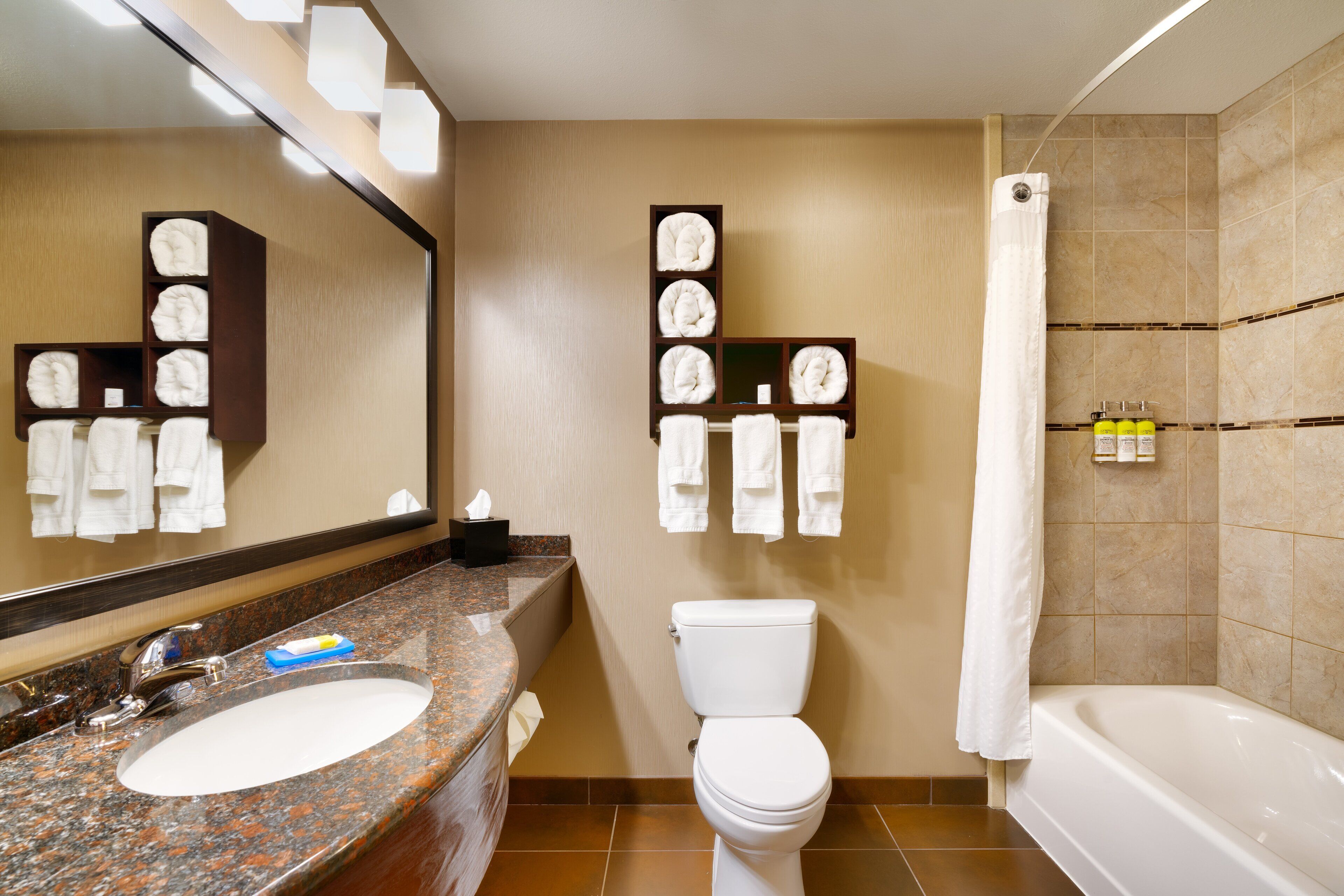A bathroom with a granite countertop sink, a white toilet, a bathtub, and towel racks with towels.