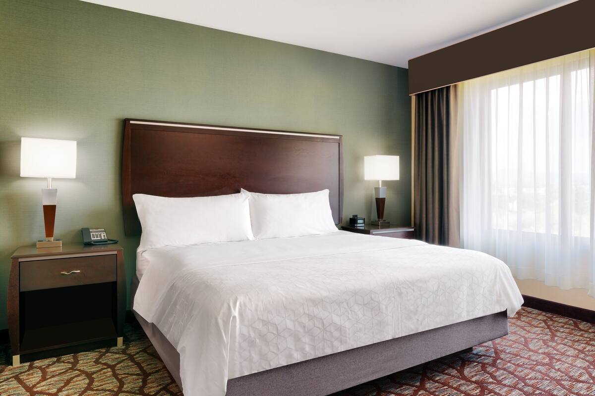A hotel room with a large bed, two bedside tables, and a window with curtains.