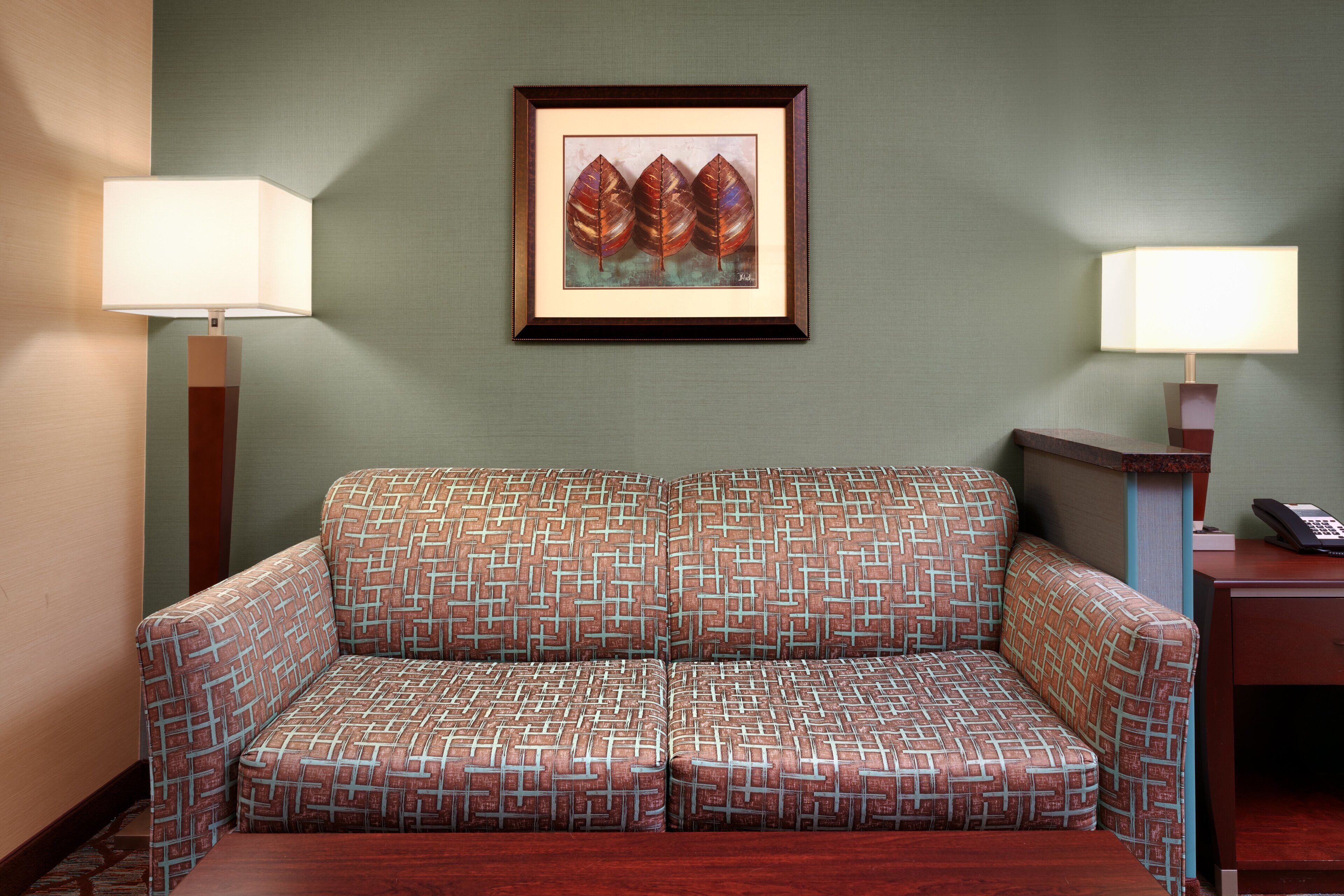 A room with a patterned sofa, two wall-mounted lamps, and a framed artwork above the sofa.