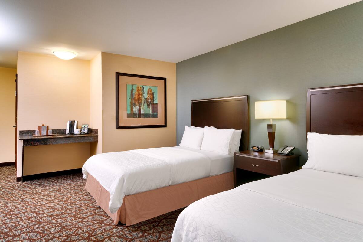 A hotel room with two beds, a desk with a lamp, a framed picture on the wall, and a patterned carpet.