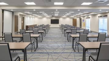 A conference room with rows of tables and chairs, a projector screen, and a carpeted floor.