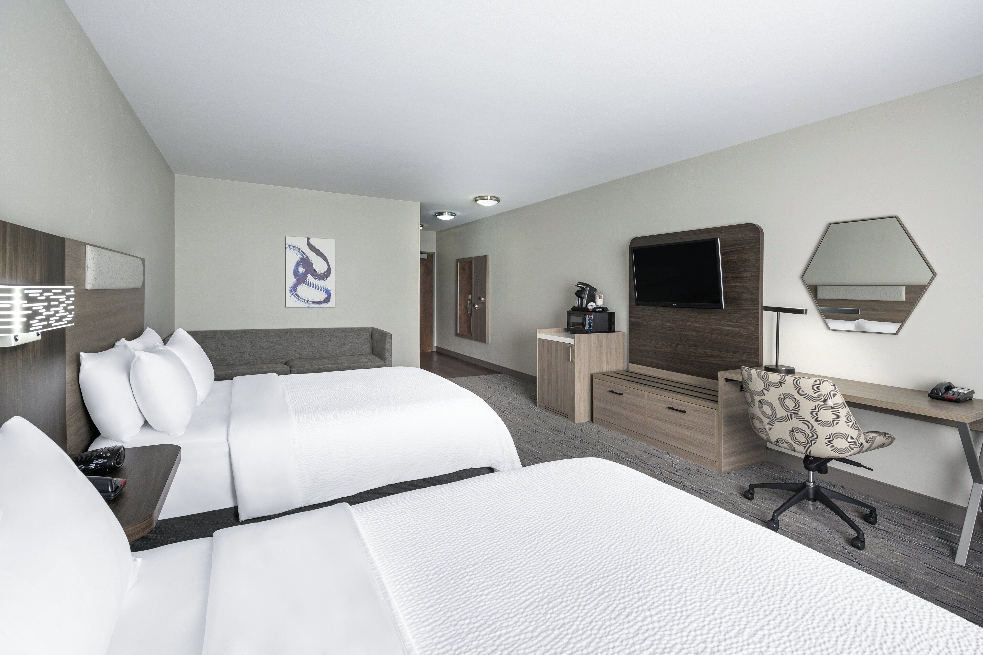 A hotel room with two beds, a desk, a chair, a TV, and a mirror.