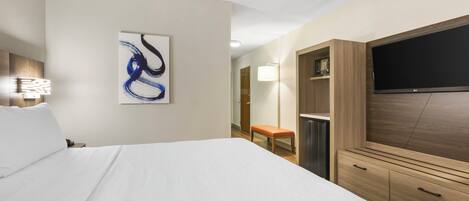 Habitación de hotel con una cama, un televisor montado en la pared, una lámpara de noche, un armario de madera y un cuadro.