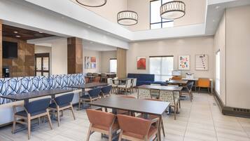 A spacious indoor area with multiple seating arrangements including tables and chairs, a large sofa, and a television mounted on the wall.