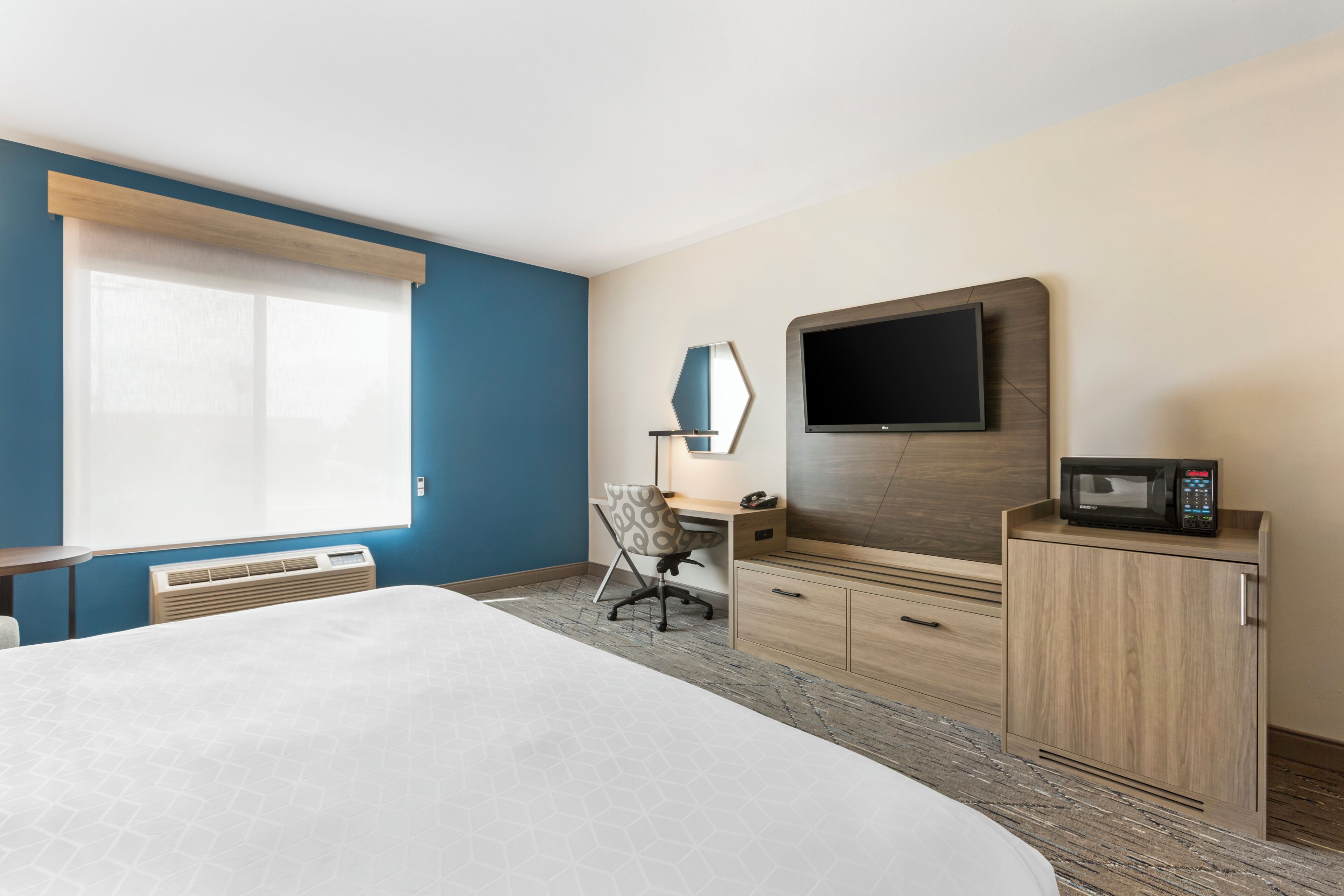 Quarto de hotel com uma cama, uma escrivaninha, uma cadeira, uma televisão e um micro-ondas.