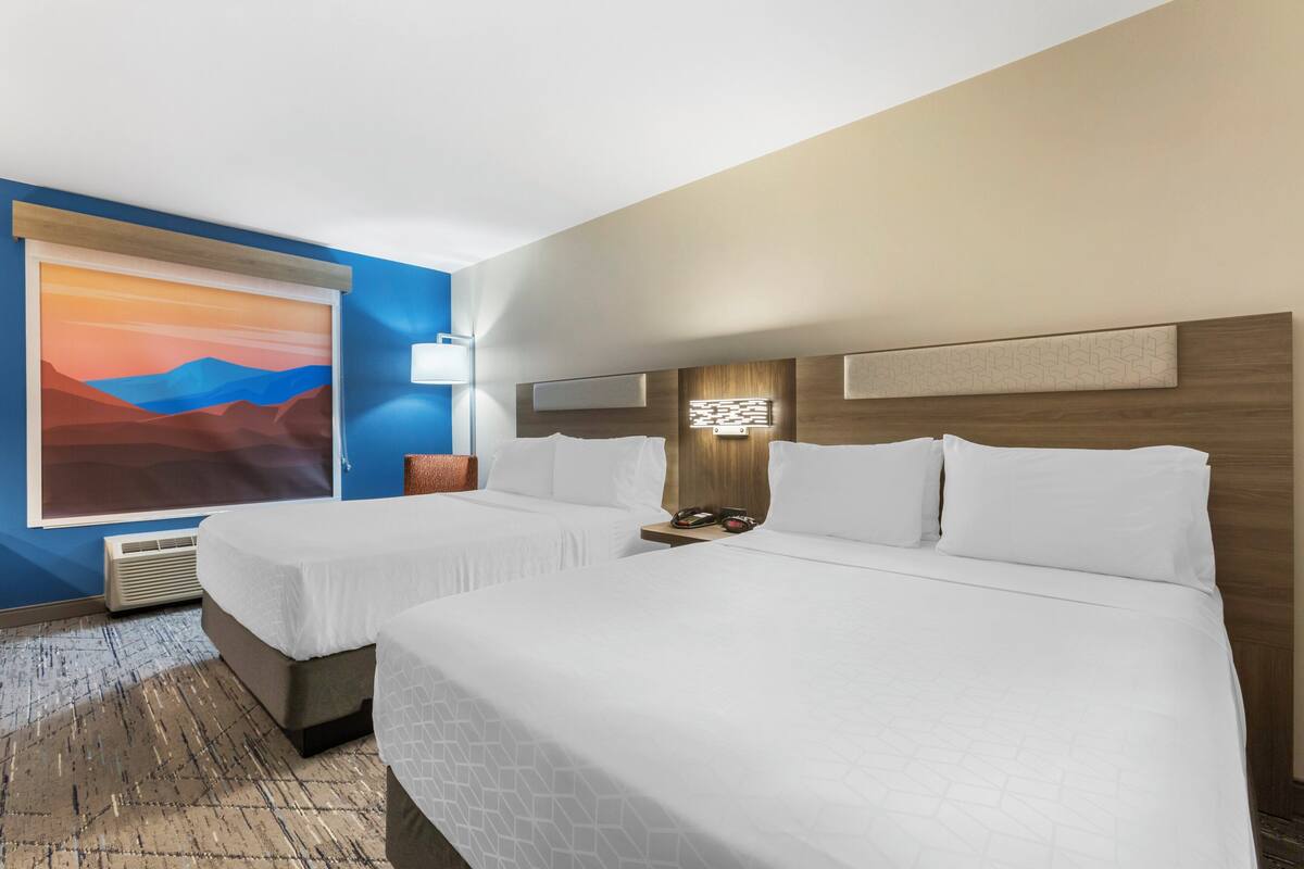 A hotel room with two beds, a large painting on the wall, a modern light fixture, and a built-in heater.