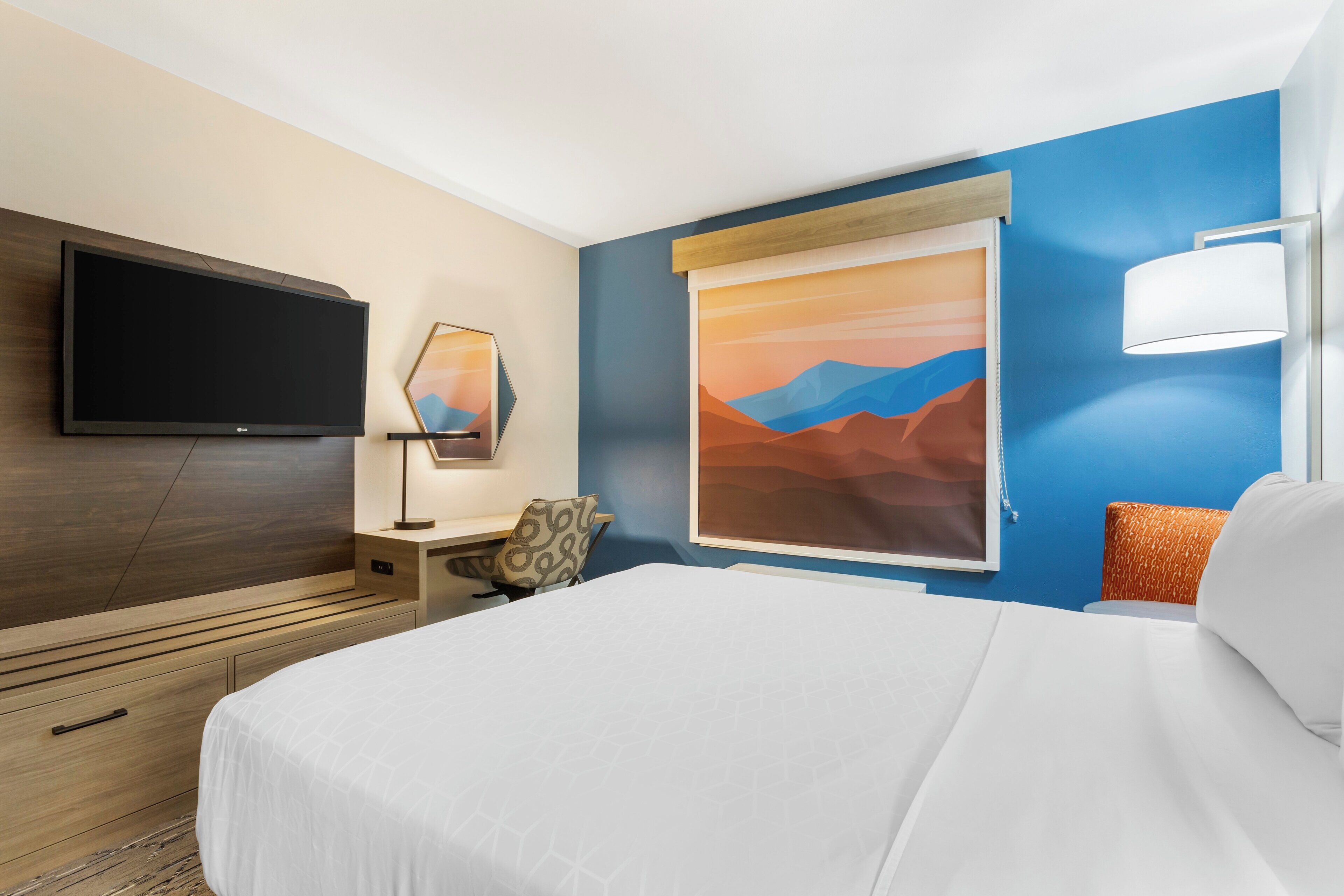 Une chambre d’hôtel équipée d’un lit, d’un téléviseur à écran plat, d’un bureau avec une chaise, d’un tableau et d’une fenêtre donnant sur les montagnes.