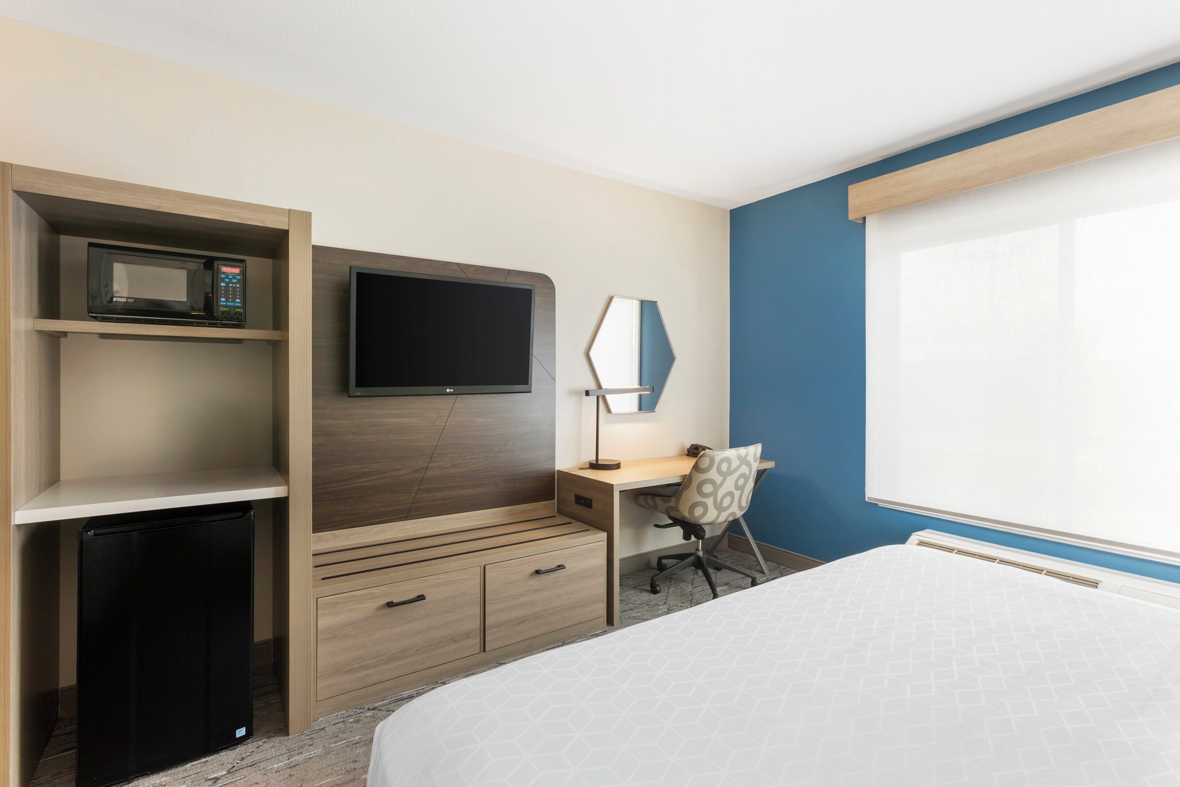 A hotel room with a bed, a desk with a chair, a TV, a microwave, and a mini fridge.