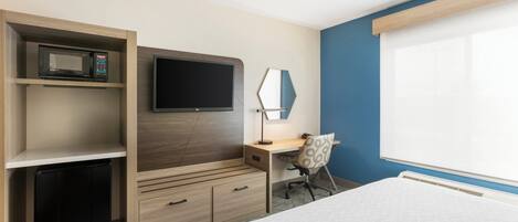 A hotel room with a bed, a desk with a chair, a TV, a microwave, and a mini fridge.