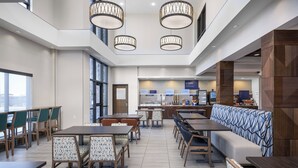 A modern dining area with multiple tables and chairs, a central seating area with a patterned sofa, and a kitchen counter in the background. - Holiday Inn Express Hotel & Suites Belgrade by IHG (Belgrade)