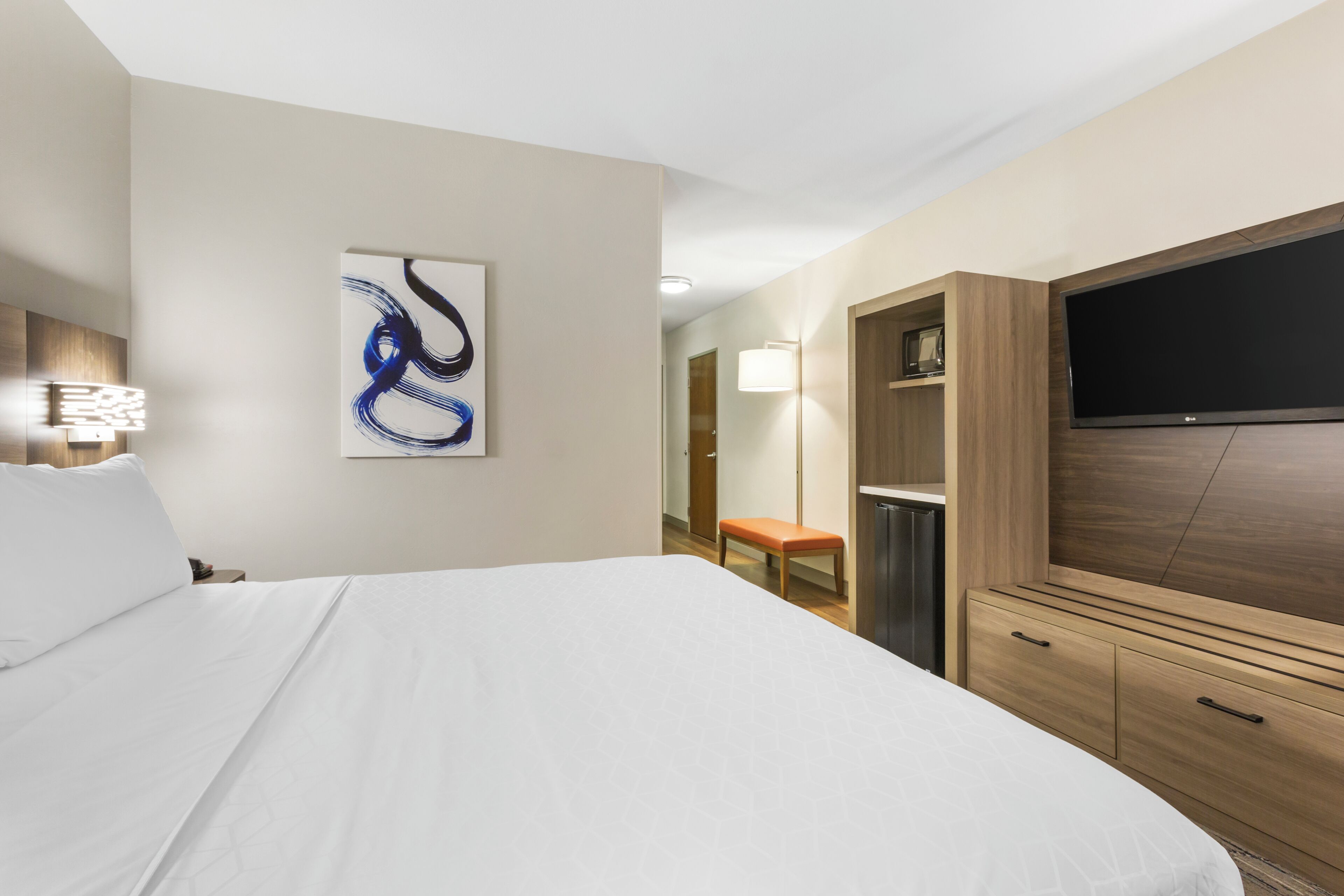 Habitación de hotel con una cama grande, un televisor de pantalla plana en la pared, un aparador de madera y un cuadro en la pared.