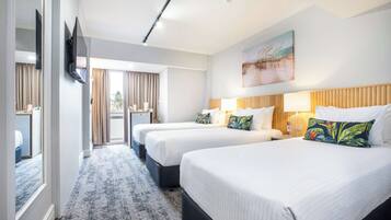 Una habitación de hotel con tres camas, un televisor, un cuadro y vistas al exterior.