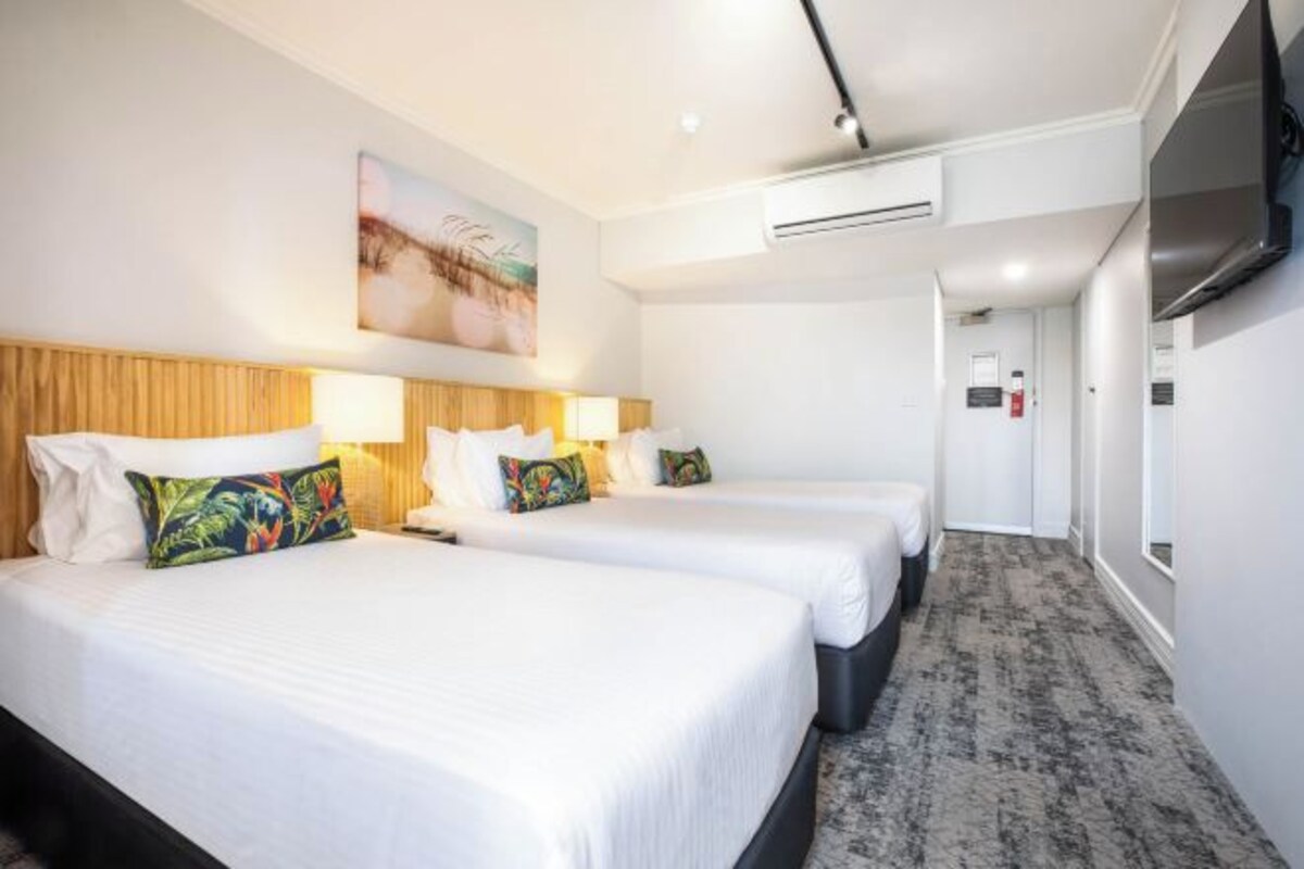 A hotel room with two beds, a wooden headboard, a painting, an air conditioning unit, and a TV.