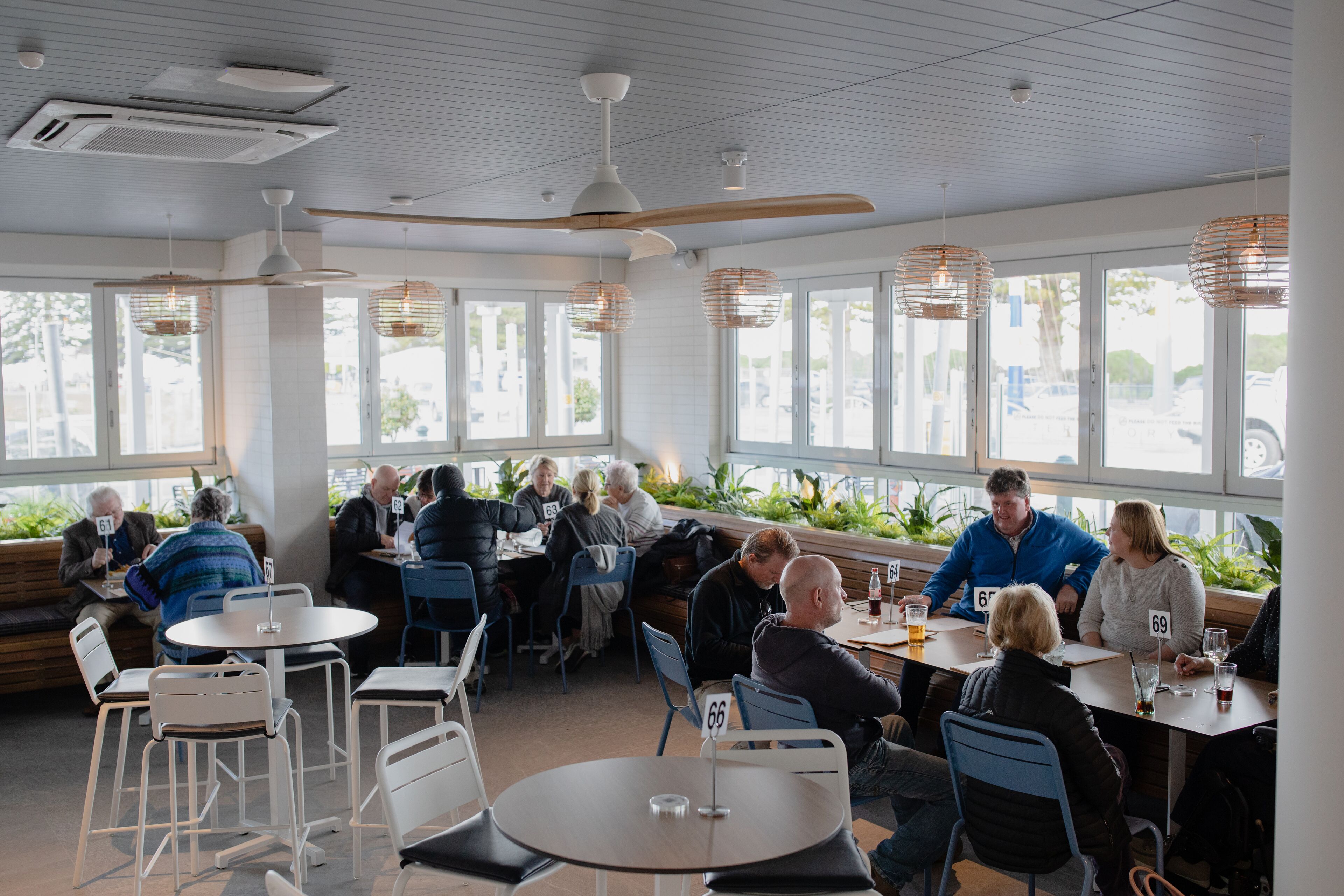 Een restaurant met ronde tafels en stoelen, grote ramen en hanglampen.