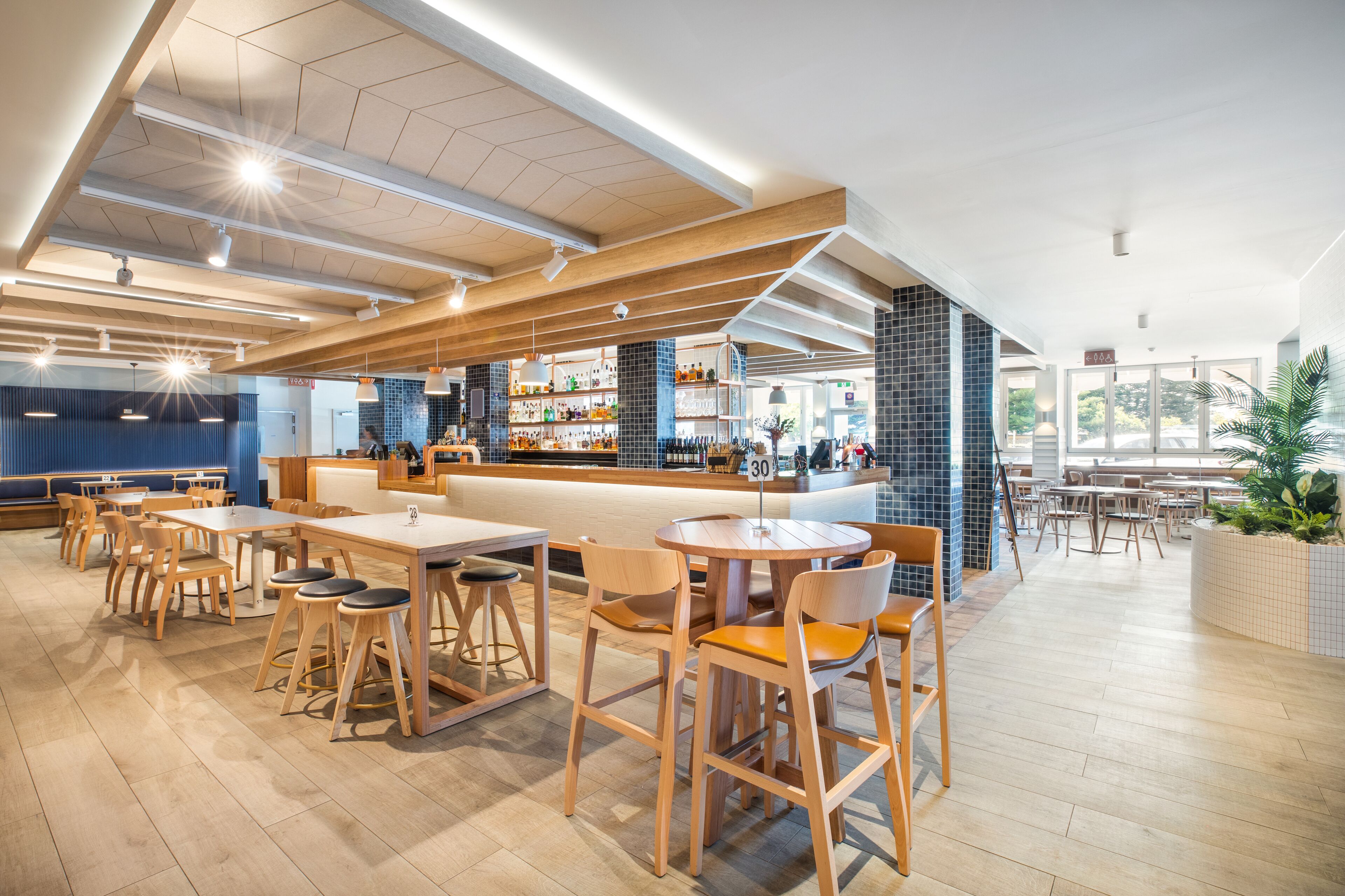 Un restaurant moderne avec des tables et des chaises en bois, un bar et une vue sur l’extérieur.