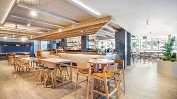 Un restaurant moderne avec des tables et des chaises en bois, un bar et une vue sur l’extérieur.