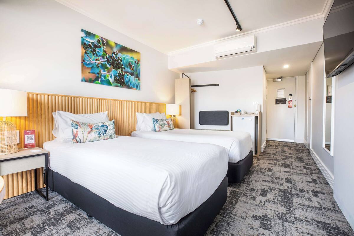 A hotel room with two beds, a desk, a TV, and a painting on the wall.