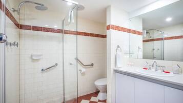 A bathroom with a glass shower enclosure, a white sink with red soap dispensers, and a toilet.