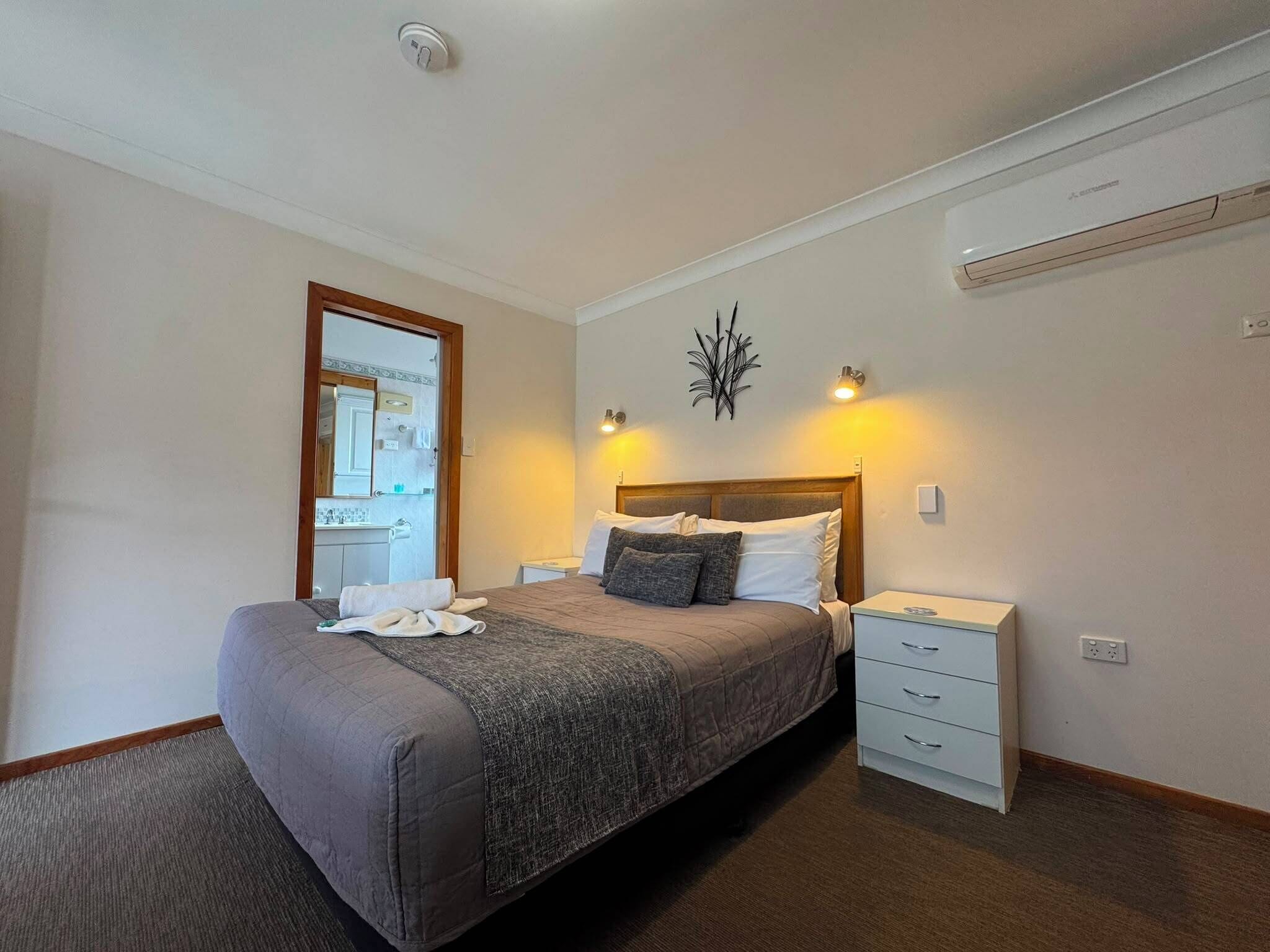 A bedroom with a bed, bedside tables, a mirror, and an air conditioning unit.