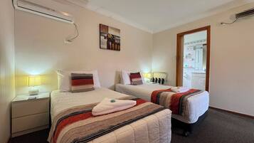 A hotel room with two beds, a nightstand with a lamp, a painting on the wall, and an air conditioning unit.