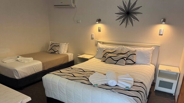 A hotel room with two beds, a desk, and a wall-mounted air conditioner.