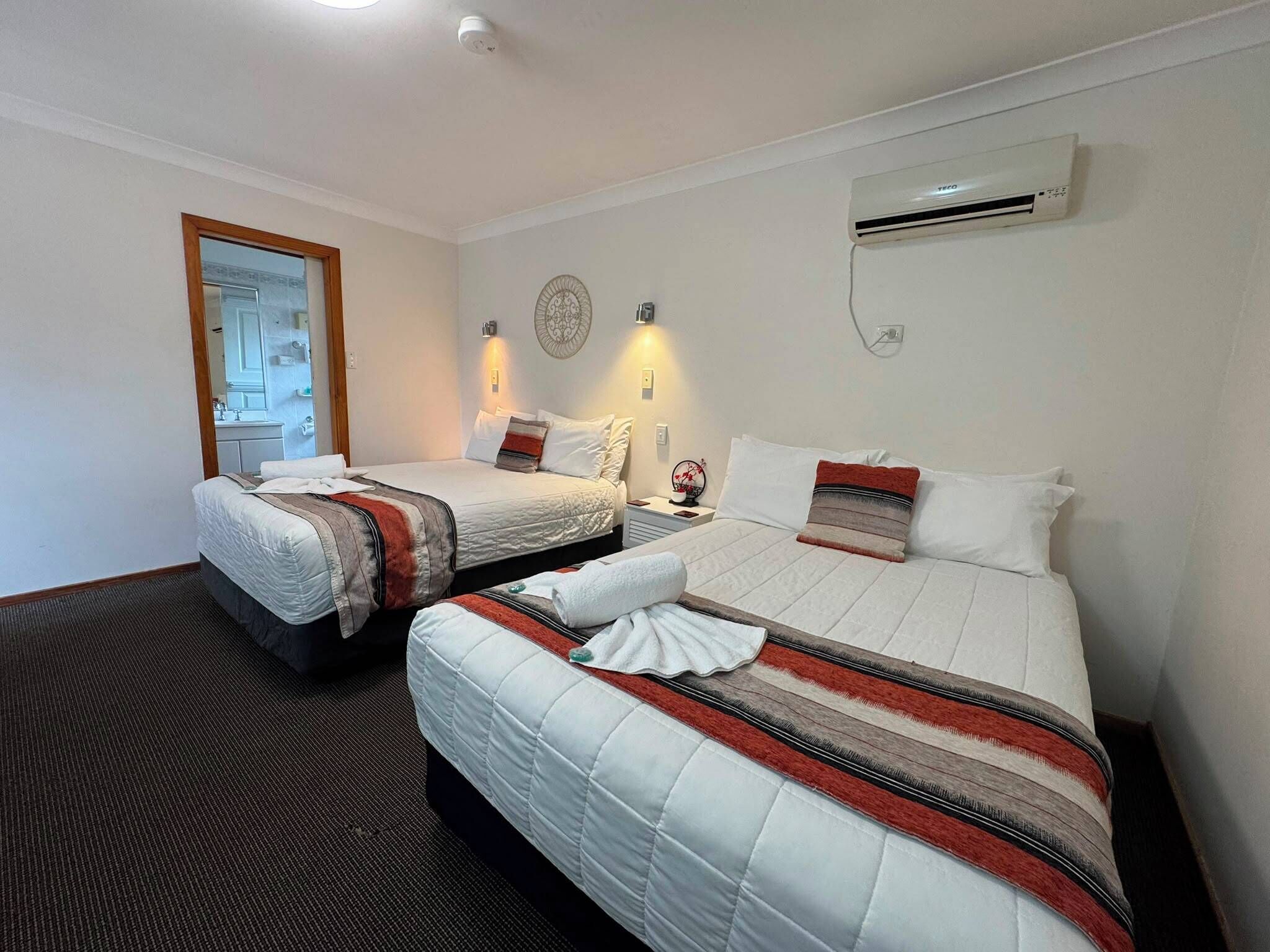 Habitación de hotel con dos camas, un espejo, un equipo de aire acondicionado y un plato decorativo en la pared.