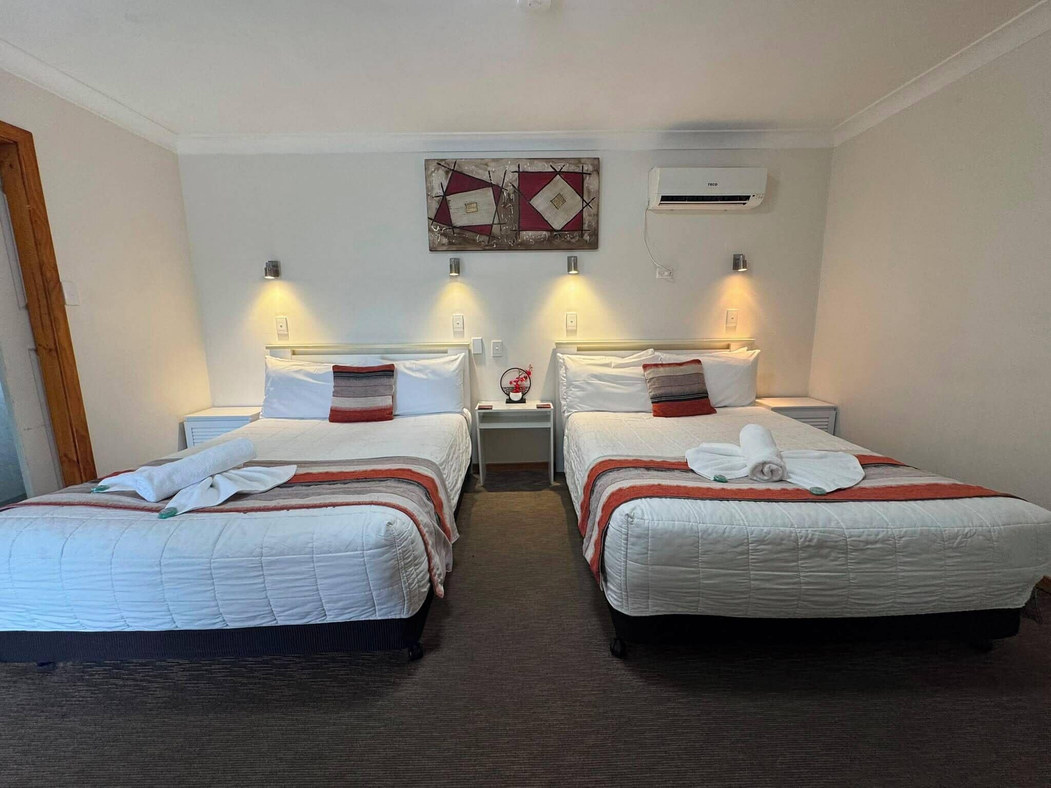 A hotel room with two beds, a wall-mounted air conditioner, and a decorative piece above the beds.