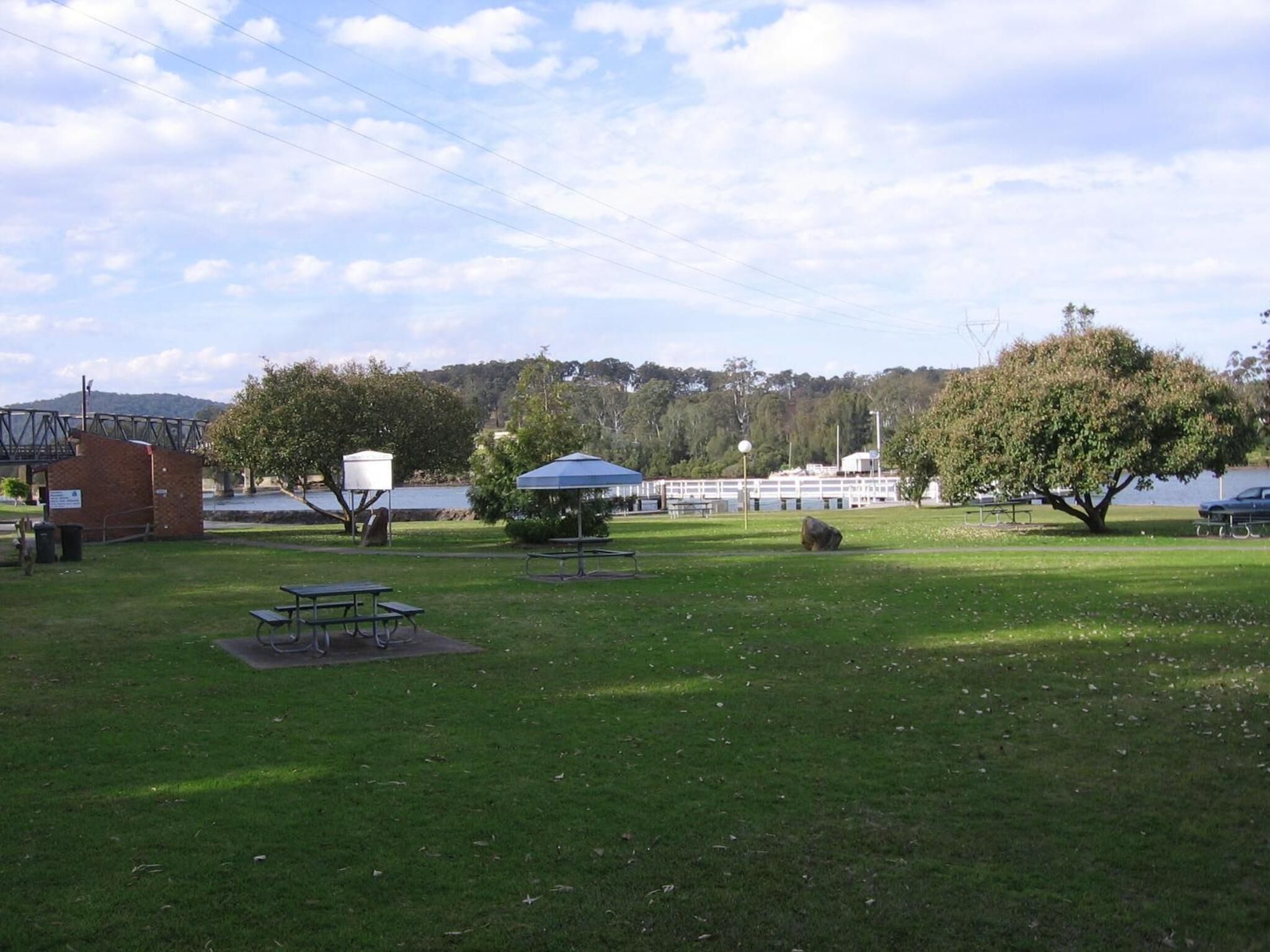 A park with picnic tables, a shelter, and a lake in the background.