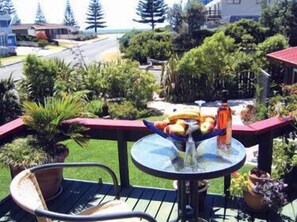 A deck with a table and chairs, surrounded by potted plants and a view of the ocean. - Moanarua Beach Cottage (Ohope)