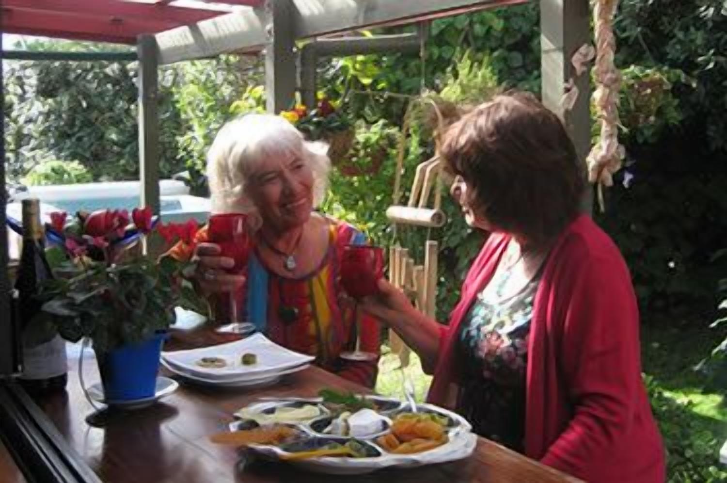 Twee personen aan een tafel met eten en drinken, omringd door groen.