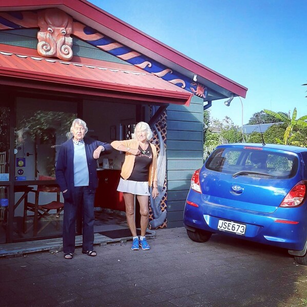 A building with a red roof and a blue car parked outside. - Moanarua Beach Cottage (Ohope)