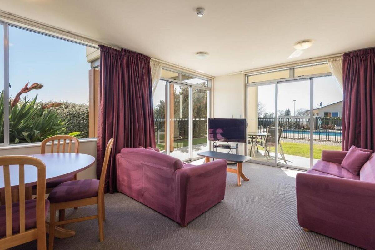 Un espacio habitable amplio con sofá, mesa de comedor y sillas. Se ve un televisor y una piscina a través de puertas de cristal.