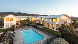 Un hotel moderno de varios pisos con piscina, rodeado de jardines cuidados y vistas a colinas.
