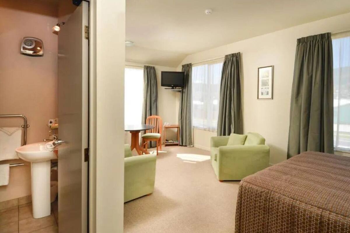Habitación de hotel con cama, un pequeño escritorio con silla, sofá, televisión y baño con lavamanos e inodoro.