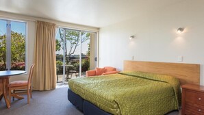 Habitación de hotel con cama, escritorio y silla. Cuenta con una puerta corrediza de vidrio que da a un espacio exterior con mesa y sillas.